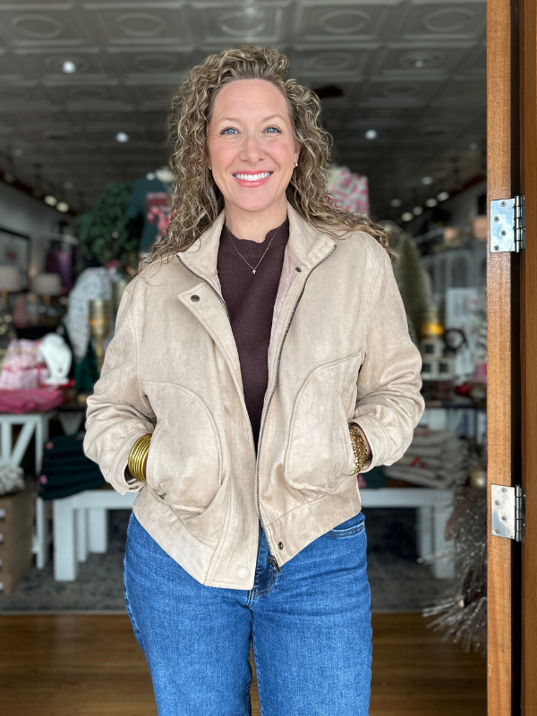 Woman wearing a beige jacket and blue jeans standing indoors.