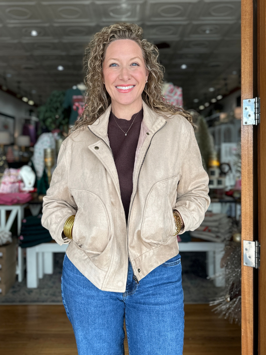Woman wearing a beige jacket and blue jeans standing indoors.