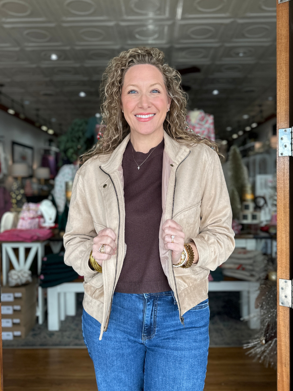 Woman wearing a beige jacket and blue jeans standing inside a store.