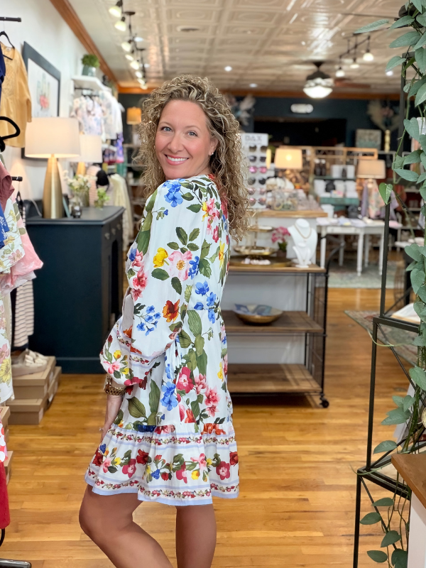 Woman in a floral dress standing in a store with wooden floors and various items on shelves.