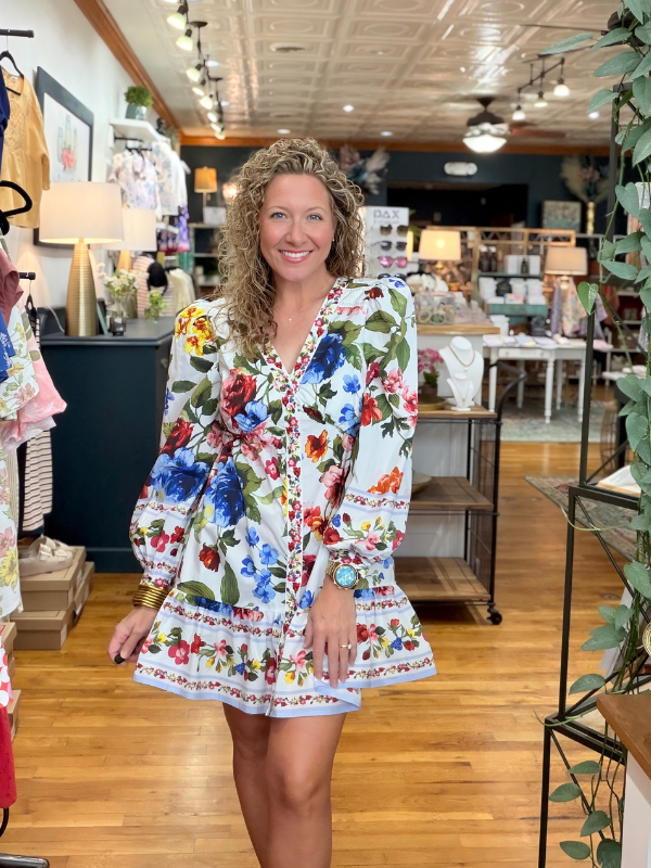 Woman in a colorful floral dress standing in a store with wooden floors and shelves.