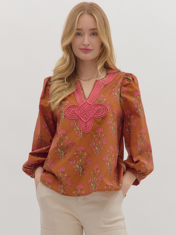 Woman wearing a patterned blouse with pink embroidery on a plain background