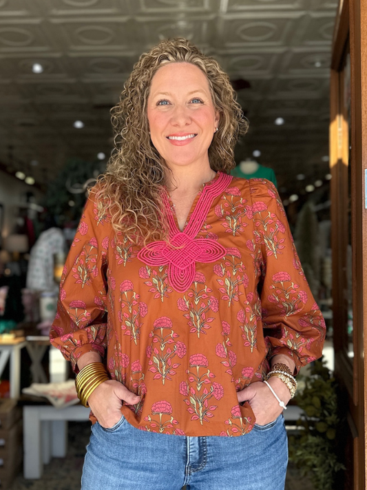 Woman wearing a patterned blouse with a pink accent in an indoor setting
