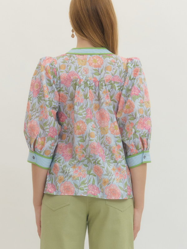 Woman wearing a floral blouse with green pants against a plain background