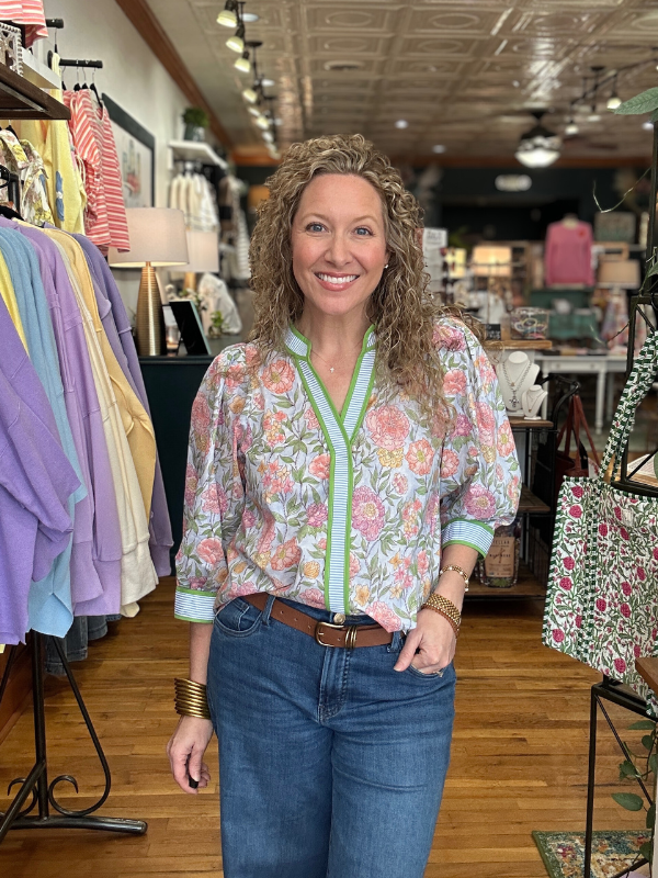 Woman in a floral blouse and jeans standing in a clothing store.