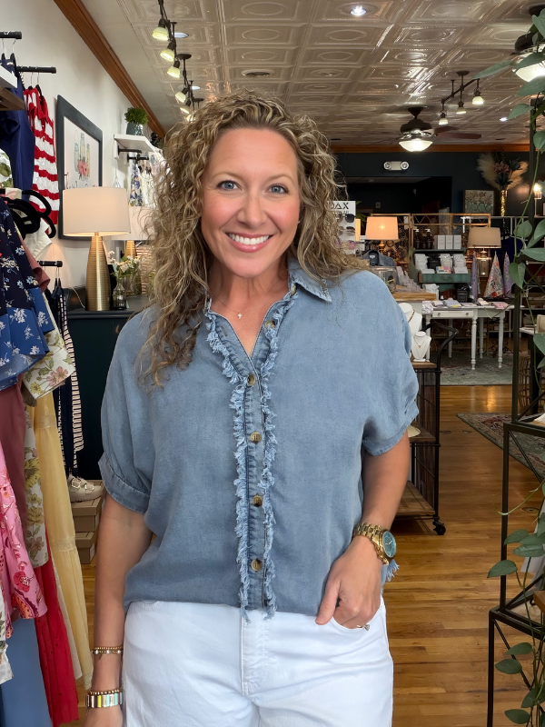 Woman in a blue shirt standing in a store with various items on display.