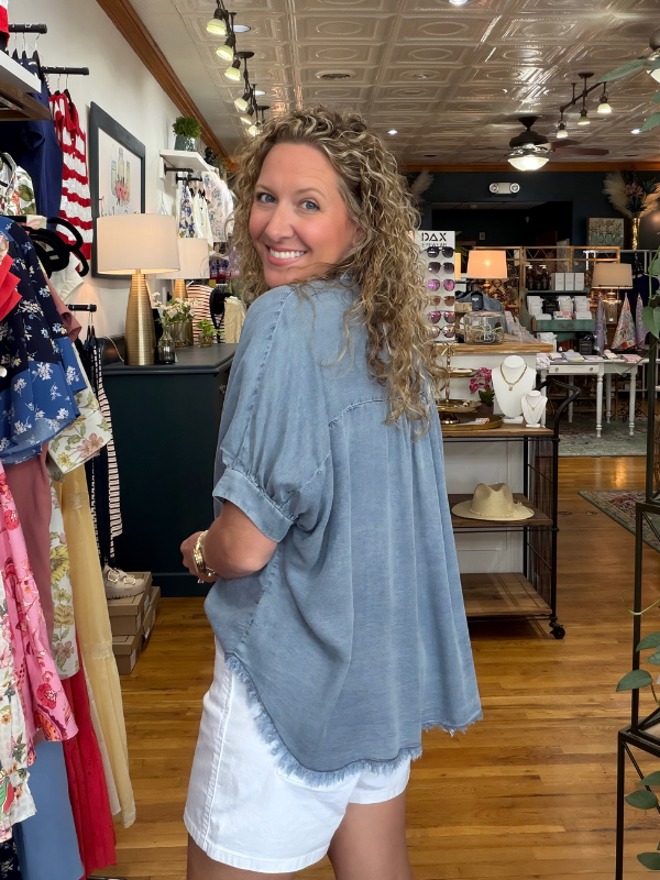 Woman in a clothing store wearing a blue shirt and white shorts, smiling.