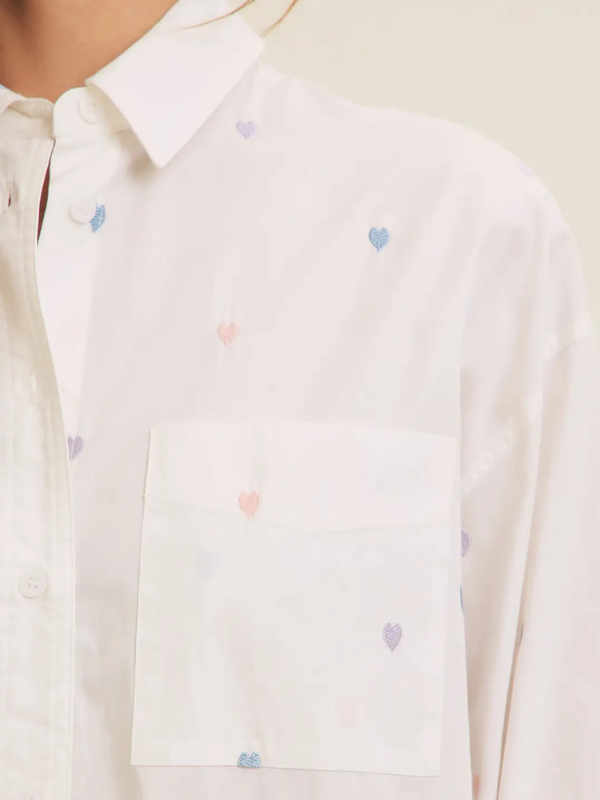 White shirt with small colorful heart patterns on a neutral background