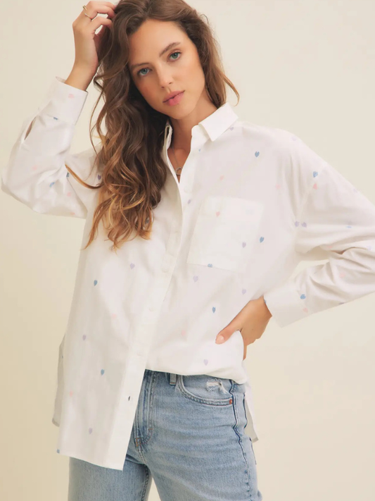 Woman wearing a white blouse with small patterns and light blue jeans against a plain background