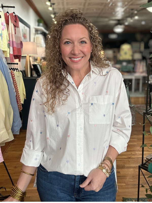 Woman wearing a white blouse with colorful patterns in a clothing store.