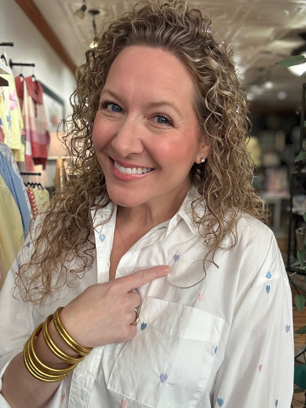 Woman pointing to a button on her white shirt in a store setting