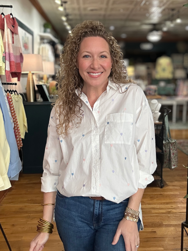 Woman wearing a white blouse with colorful patterns in a clothing store.