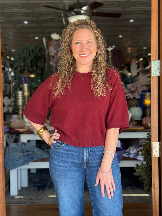Woman wearing a red sweater and blue jeans standing inside a store.