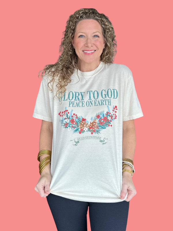 Woman wearing a white t-shirt with 'Glory to God Peace on Earth' design against a pink background