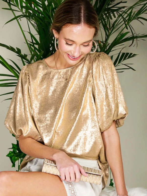 Woman wearing a gold sequin top sitting in front of green plants.