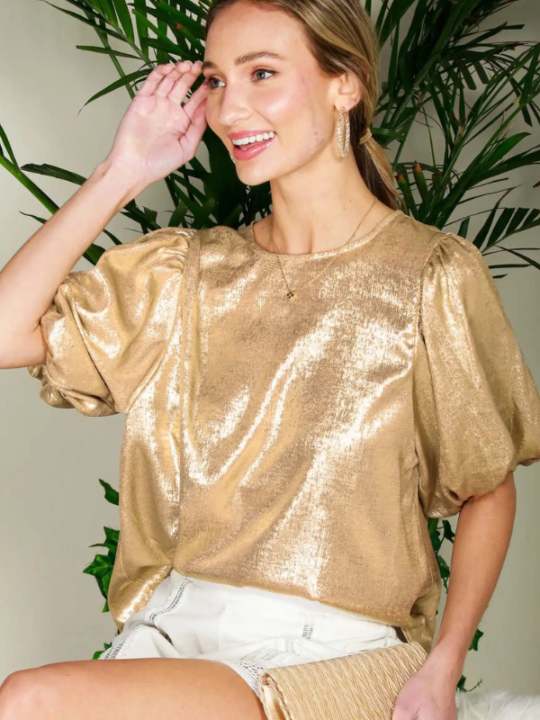 Woman wearing a gold sequin top with plants in the background