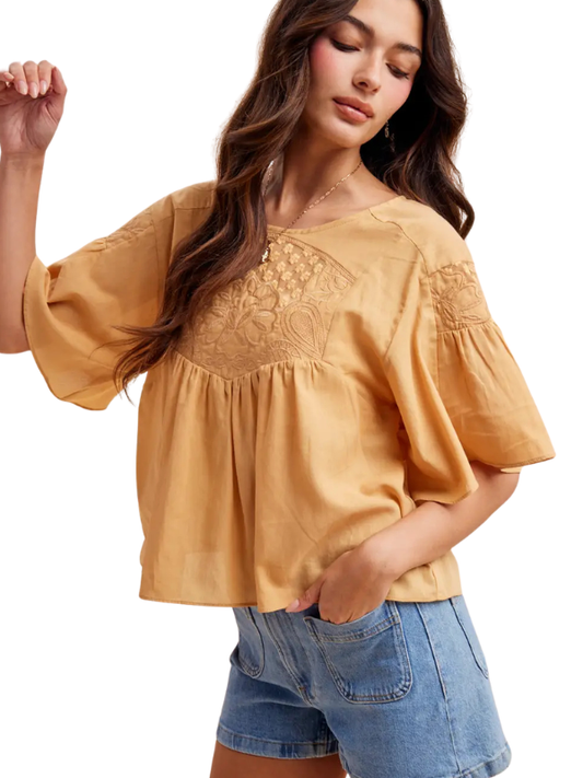 Woman wearing a mustard yellow blouse with lace details and denim shorts on a white background