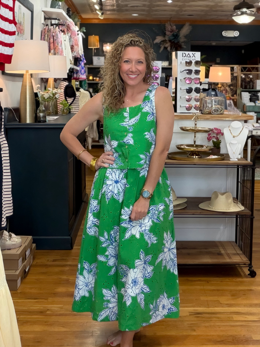 Woman in a green floral dress standing in a store with various items on display.