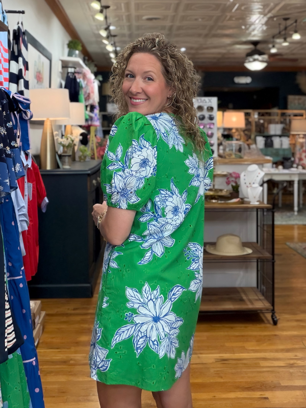 Woman wearing a green dress with blue floral patterns in a store setting.