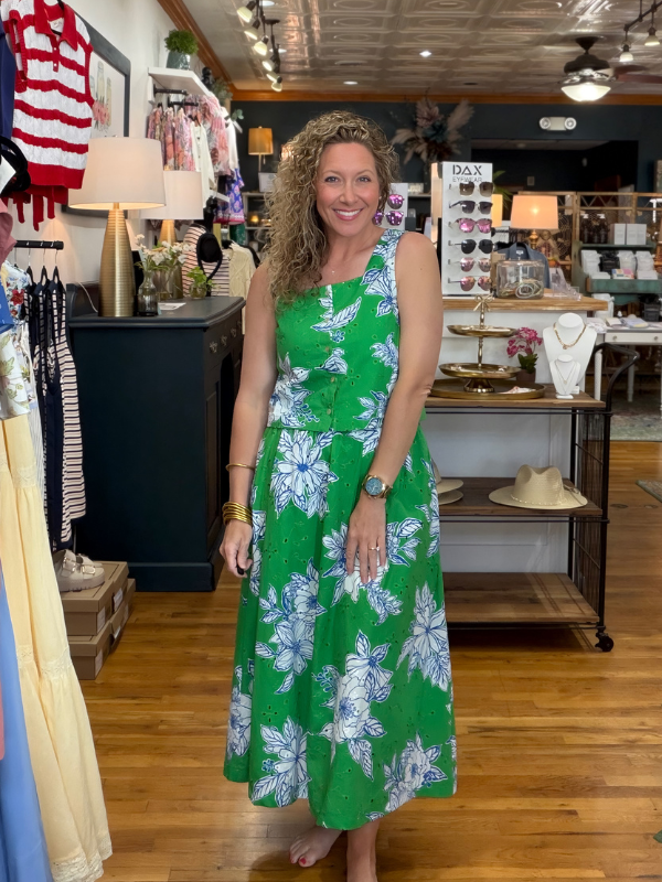 Woman in a green floral dress standing in a store with various items on display.