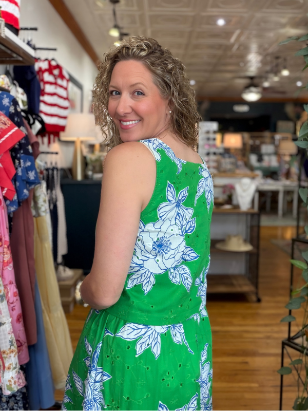 Woman in a green floral dress standing in a store with various items on display.