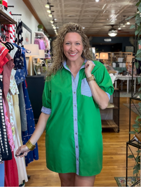 Woman wearing a green dress with a striped shirt underneath in a clothing store.