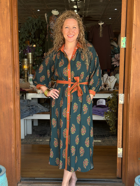 Woman wearing a green and orange patterned dress standing in a doorway.