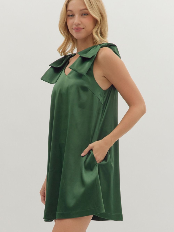 Woman wearing a green dress with a large bow on a plain background
