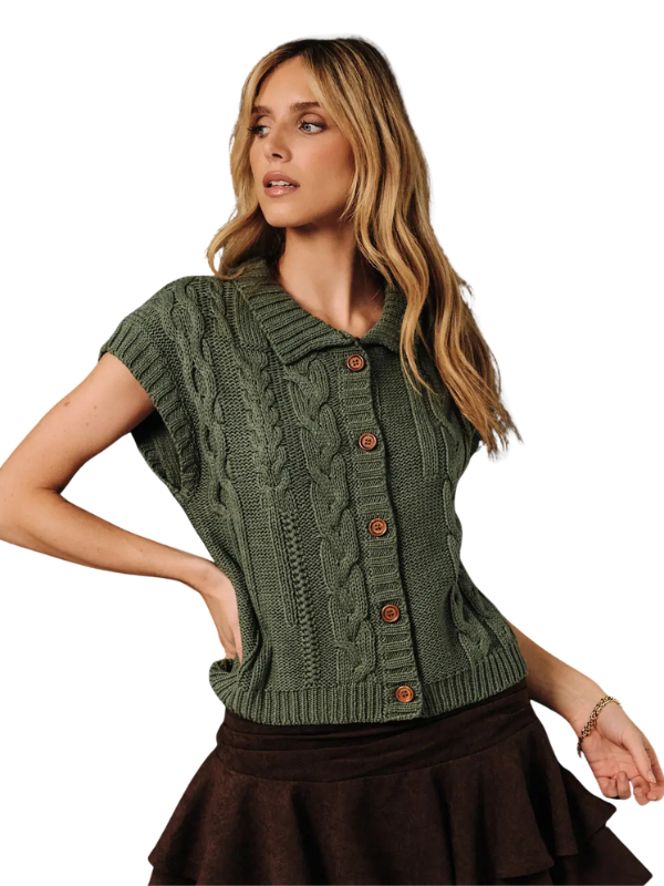 A woman wearing a short-sleeve olive green cable-knit button-front cardigan top with brown buttons, paired with a dark brown skirt, against a plain white background.
