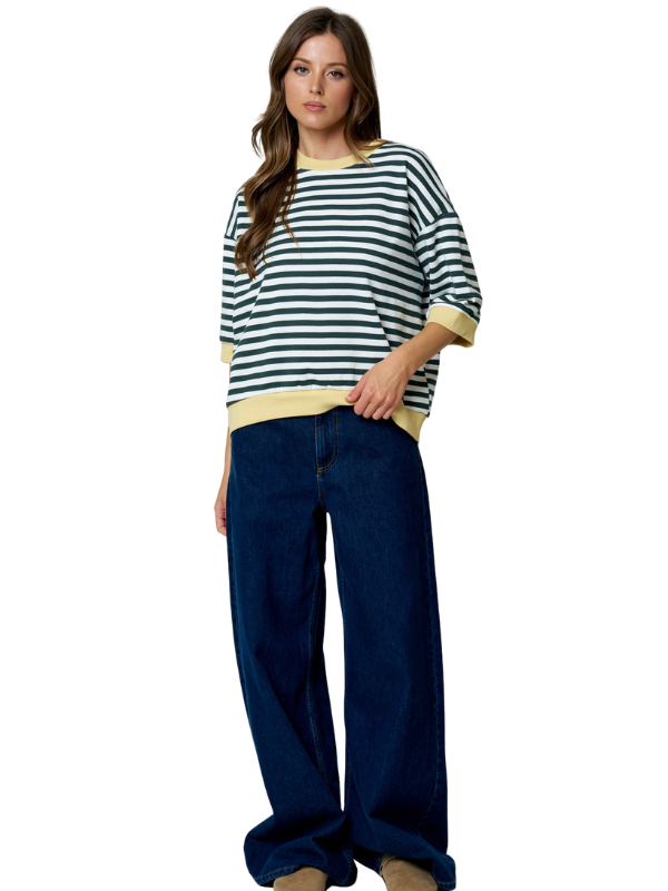 A woman modeling a navy and cream striped knit top with three-quarter sleeves and dark blue wide-leg jeans, set against a plain white background.