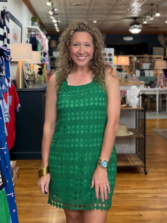 Woman in a green dress standing in a store with clothing racks and displays.