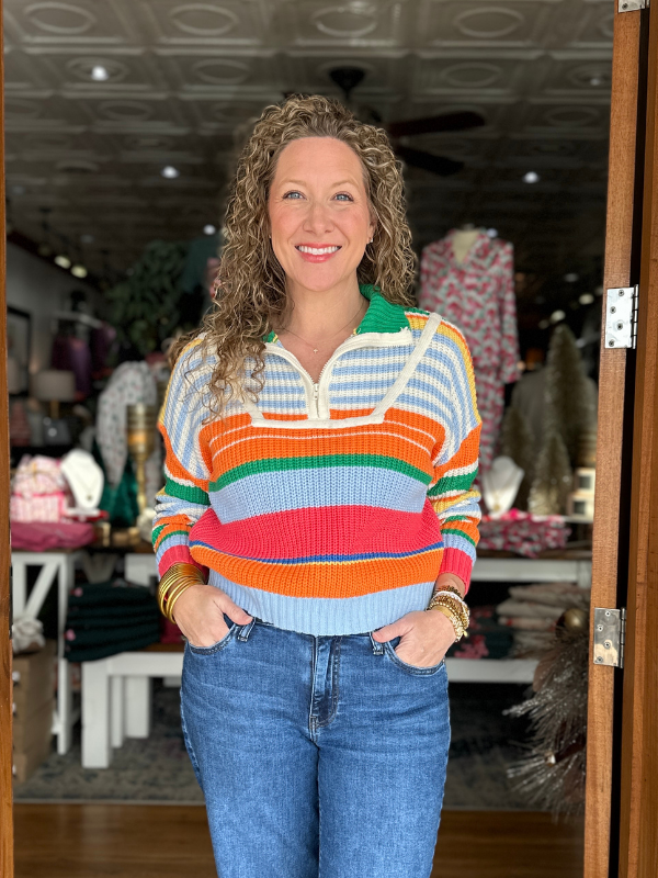 Woman wearing a colorful striped sweater and blue jeans standing in a store.