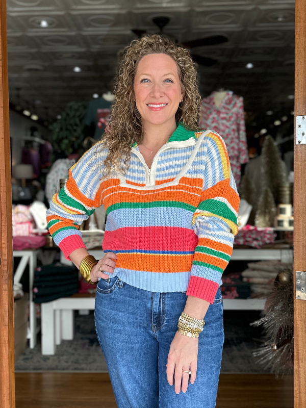 Woman wearing a colorful striped sweater and jeans in an indoor setting.
