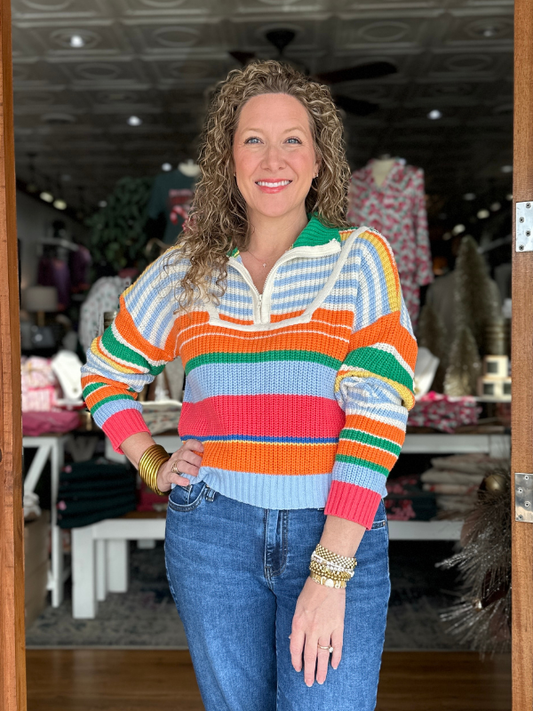 Woman wearing a colorful striped sweater and jeans in an indoor setting.