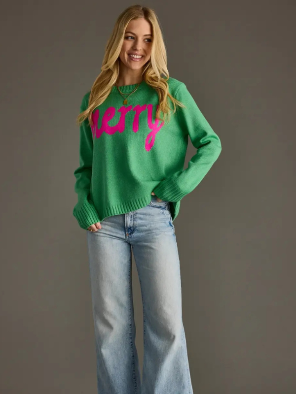 Person wearing a green sweater with pink text and blue jeans on a gray background