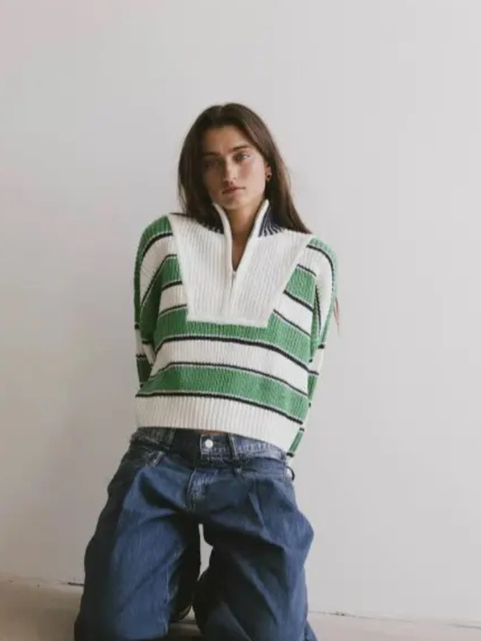 Person wearing a green and white striped sweater with blue jeans against a plain background