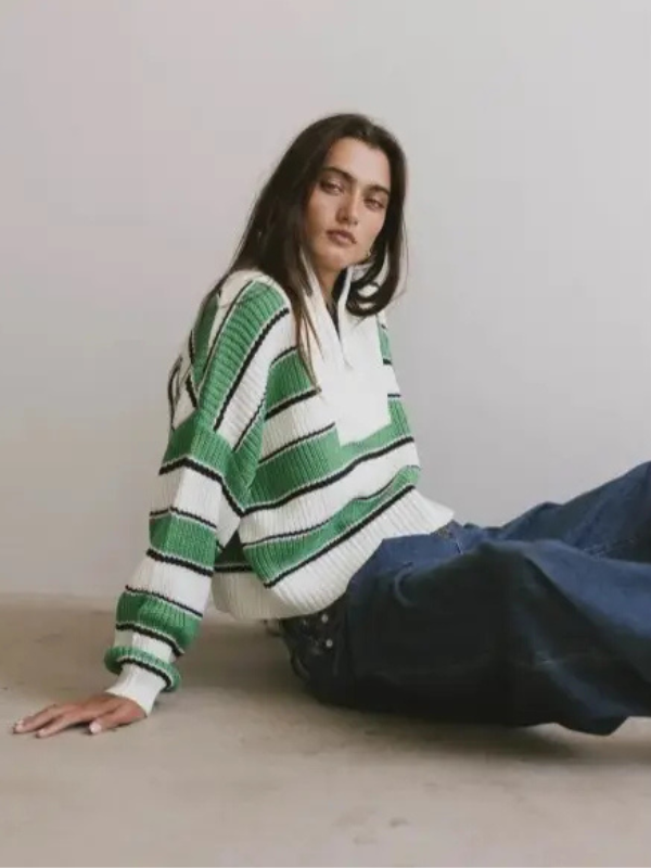 Person wearing a green and white striped sweater sitting on the floor against a plain background