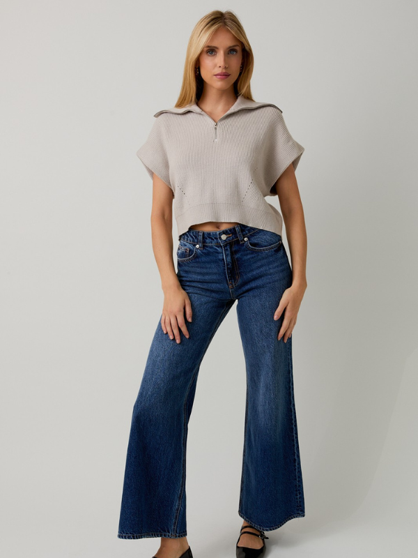 Woman wearing a beige top and blue jeans on a plain background