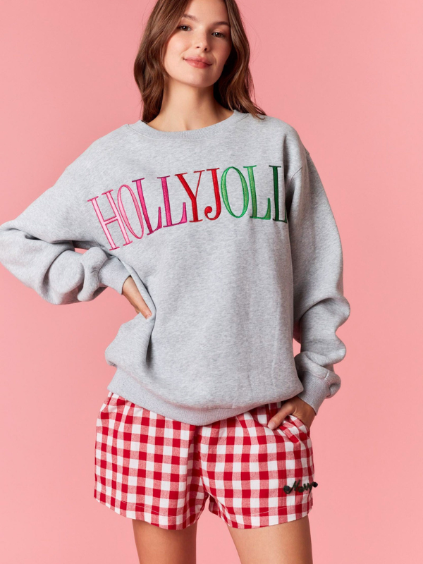 Person wearing a gray sweatshirt with 'HOLLYJOLI' and red checkered shorts on a pink background