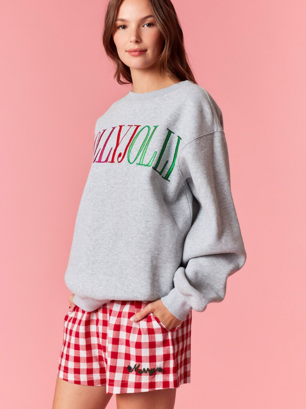 Person wearing a gray sweatshirt with 'Merry Jolly' text and red checkered shorts on a pink background