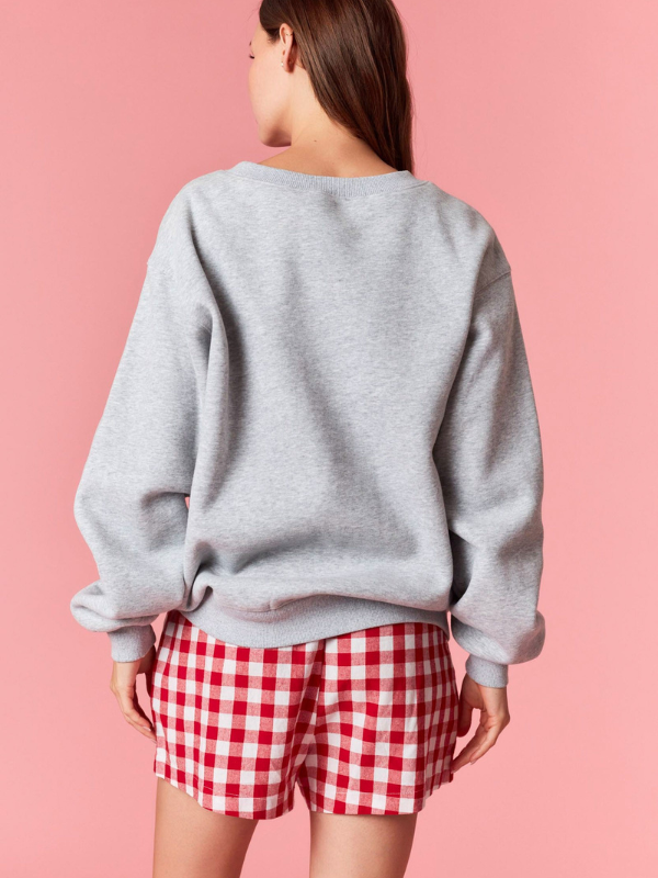 Person wearing a gray sweatshirt and red checkered shorts on a pink background