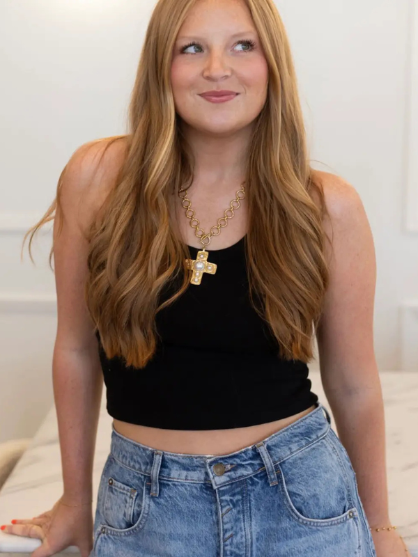 Woman wearing a black tank top and blue jeans with a gold necklace.