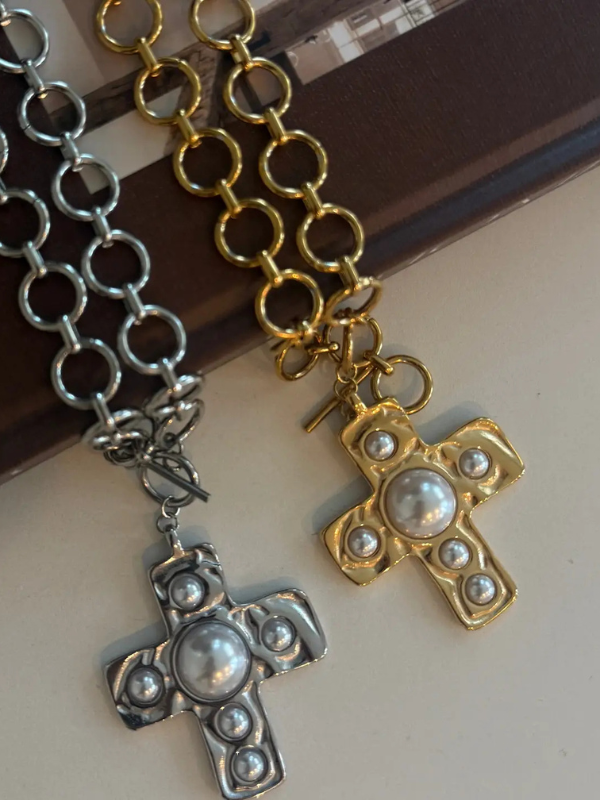 Two cross-shaped pendants, one silver and one gold, with pearl-like embellishments on a reflective surface.