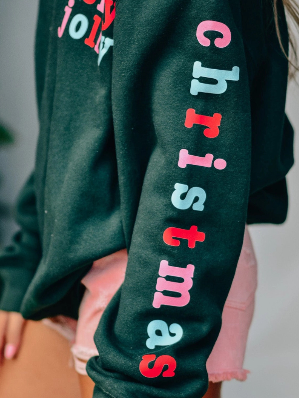 Green sweatshirt with colorful 'Christmas' text on a blurred background