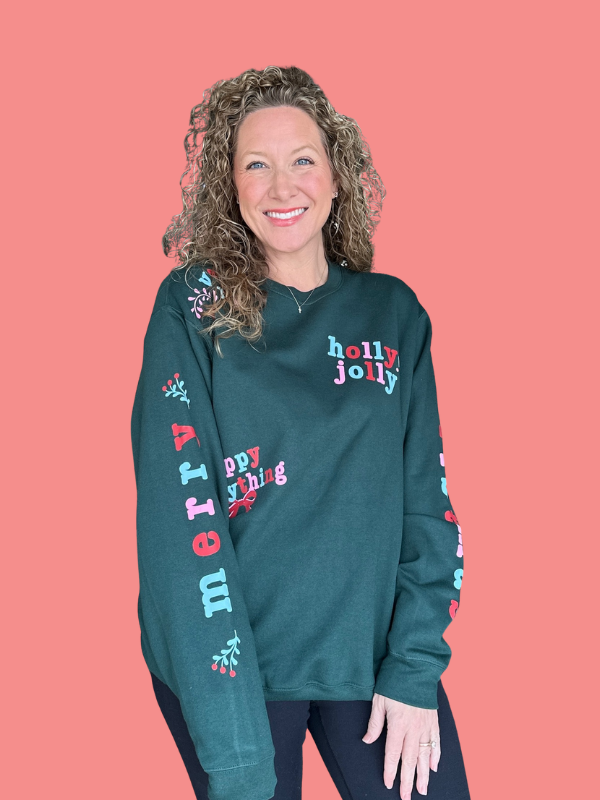 Woman wearing a green 'holly jolly' sweater against a pink background