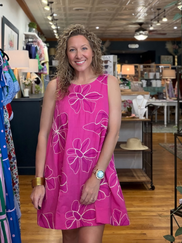 Woman wearing a pink dress with white floral patterns in a store setting.