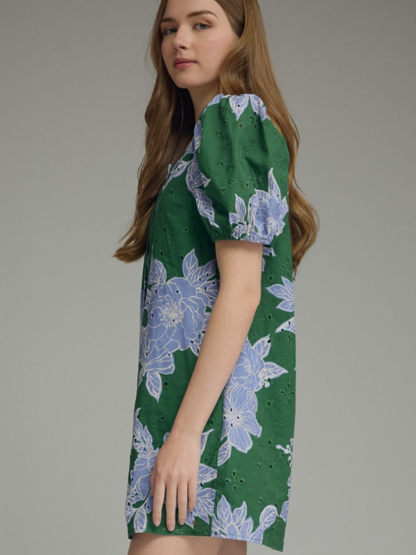 Woman wearing a green dress with blue floral pattern on a gray background