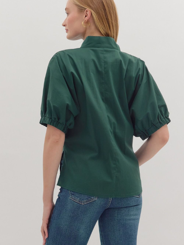 Person wearing a green blouse with short sleeves and blue jeans on a light gray background
