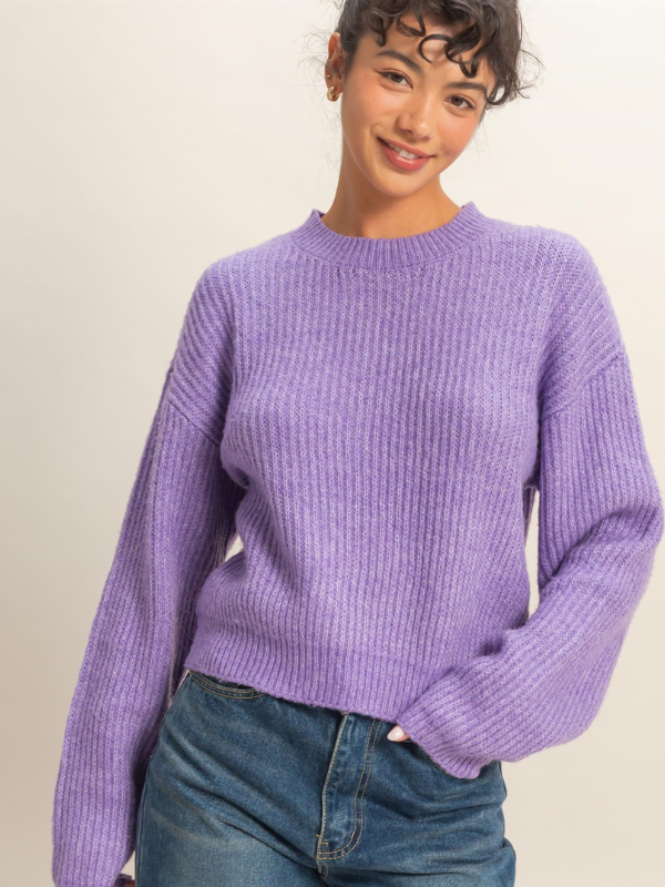 Person wearing a purple sweater and blue jeans against a plain background