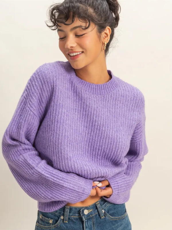 Woman wearing a purple sweater and blue jeans against a plain background